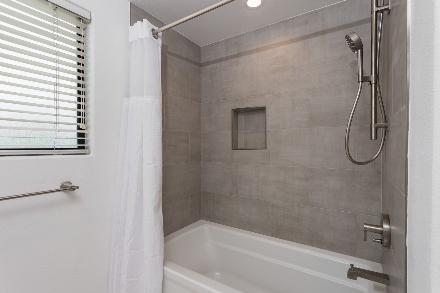 Bath and shower combination with a wall-mounted rail and a handheld shower on a slide bar
