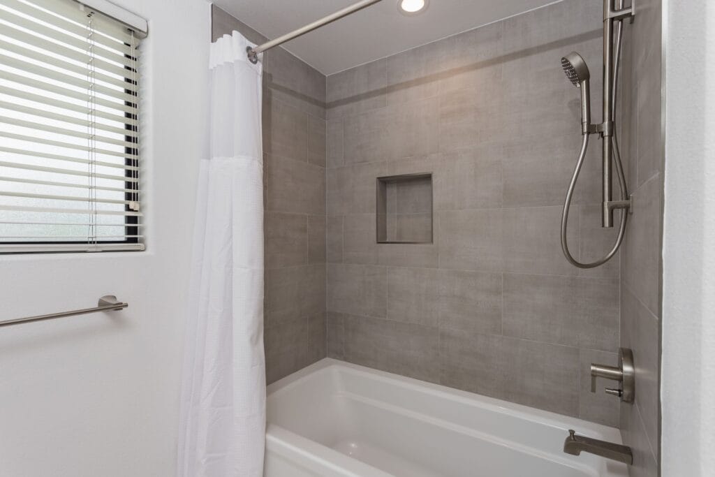 Bath and shower combination with a wall-mounted rail and a handheld shower on a slide bar