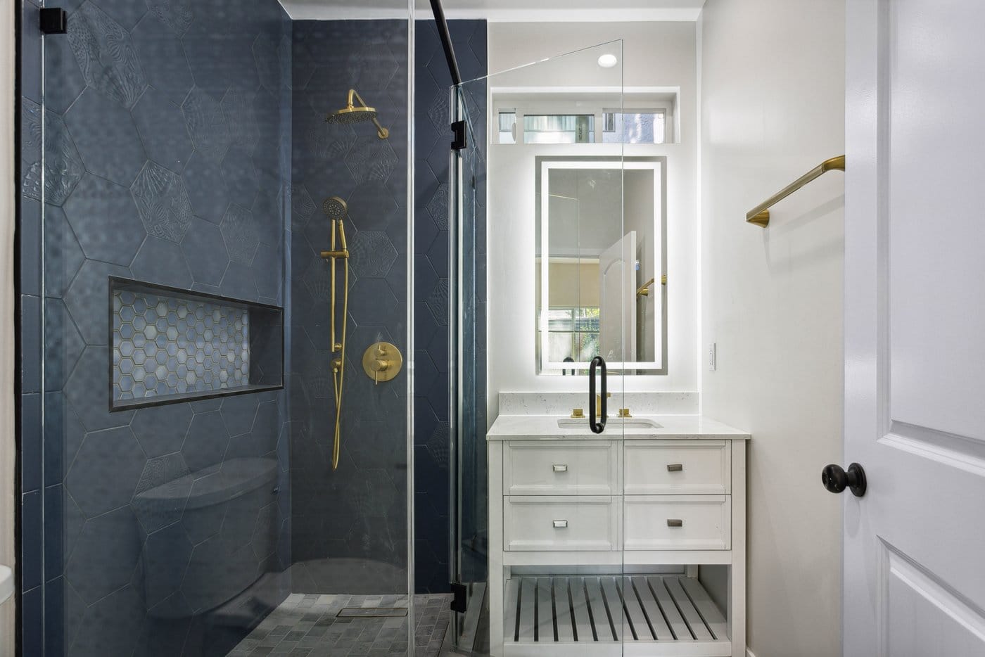 Bathroom with a navy hexagonal tiled shower behind a framed glass screen, brass fittings, a recessed niche and a white vanity