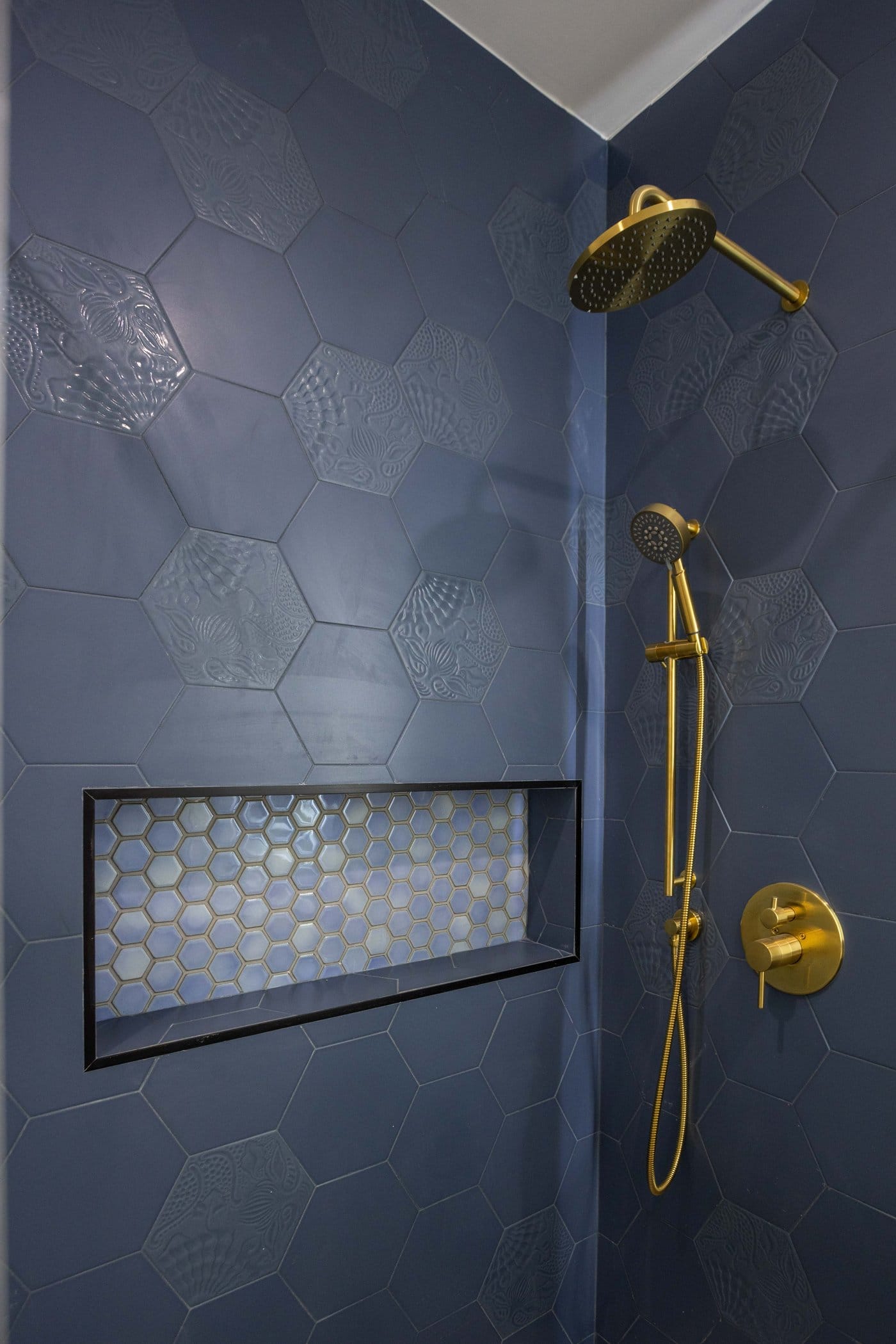 White vanity with drawers and a lit mirror beside a framed glass shower screen over navy hexagonal tile