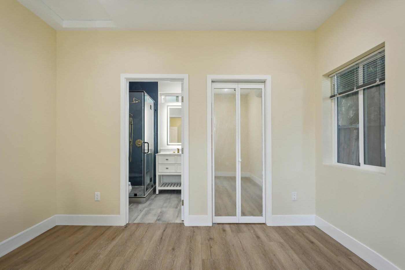 Bedroom with mirrored sliding closet doors standing open beside a doorway through to the bathroom