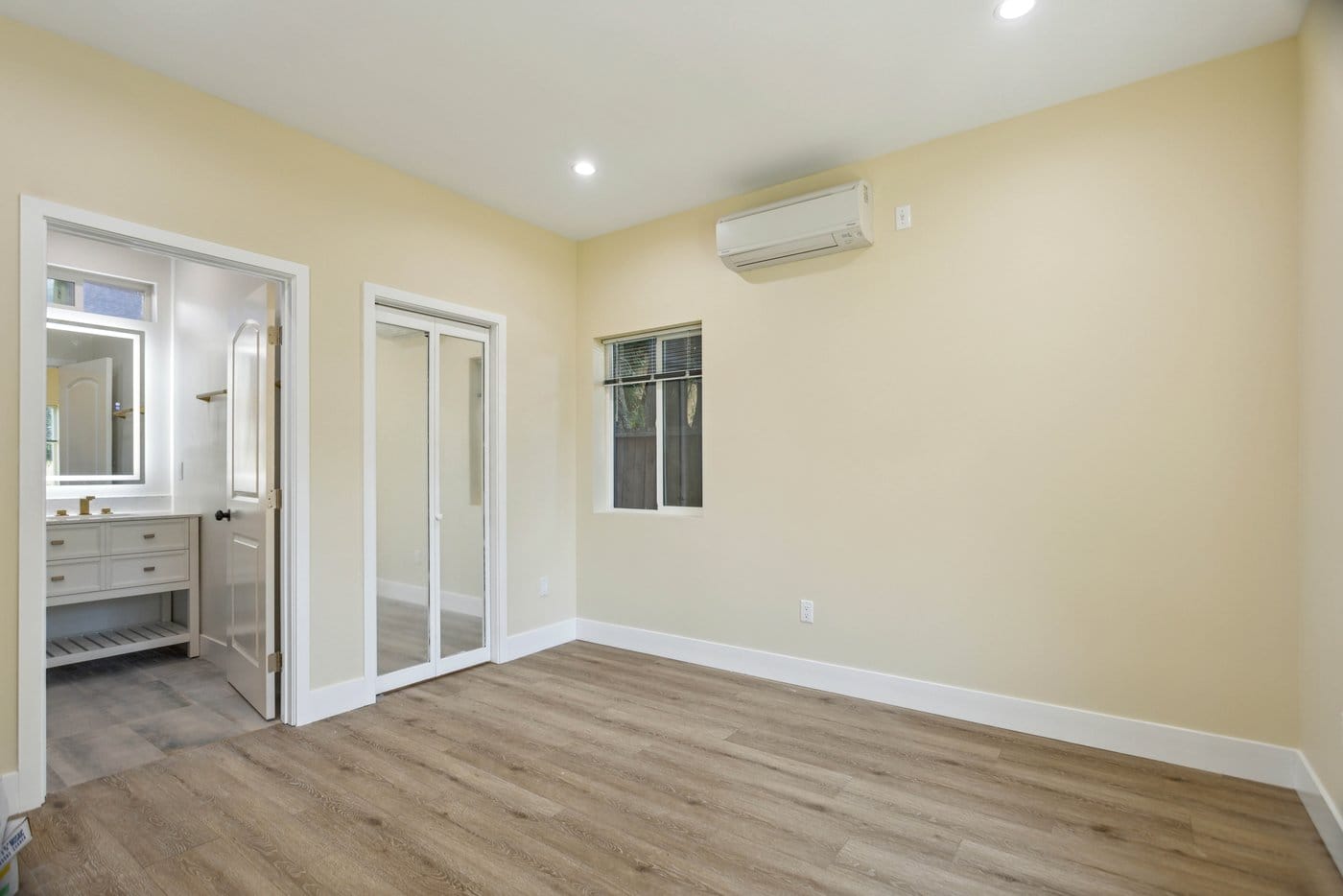 Bedroom with pale walls, a wall-mounted mini-split, a window and mirrored sliding closet doors