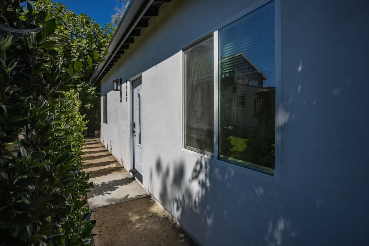 Exterior entry door to the converted unit beside a wall light, with a concrete path and hedge alongside