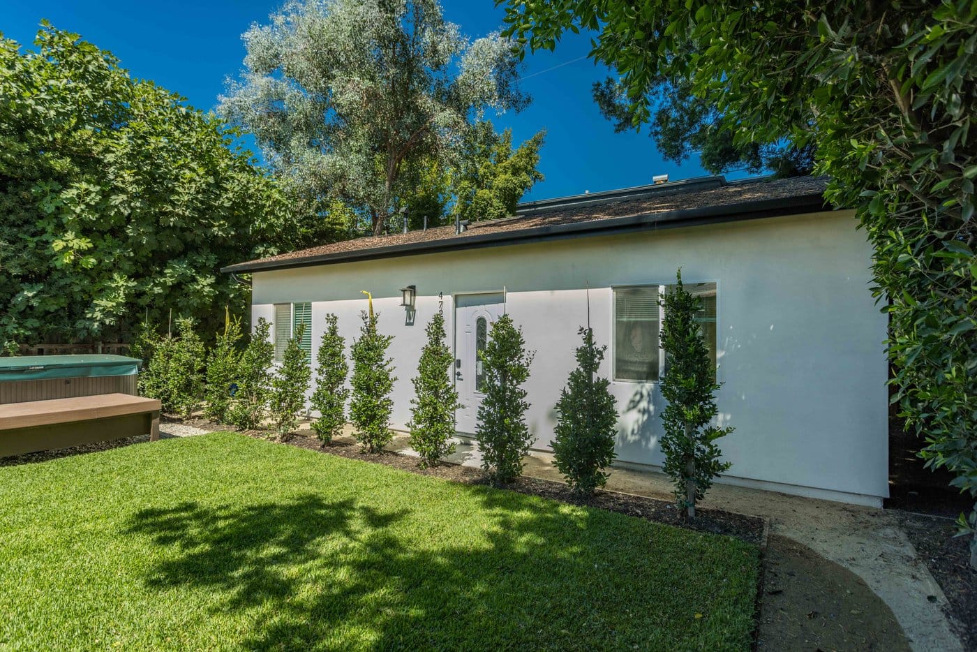 Light stucco elevation of a converted unit behind young columnar planting and a timber walkway