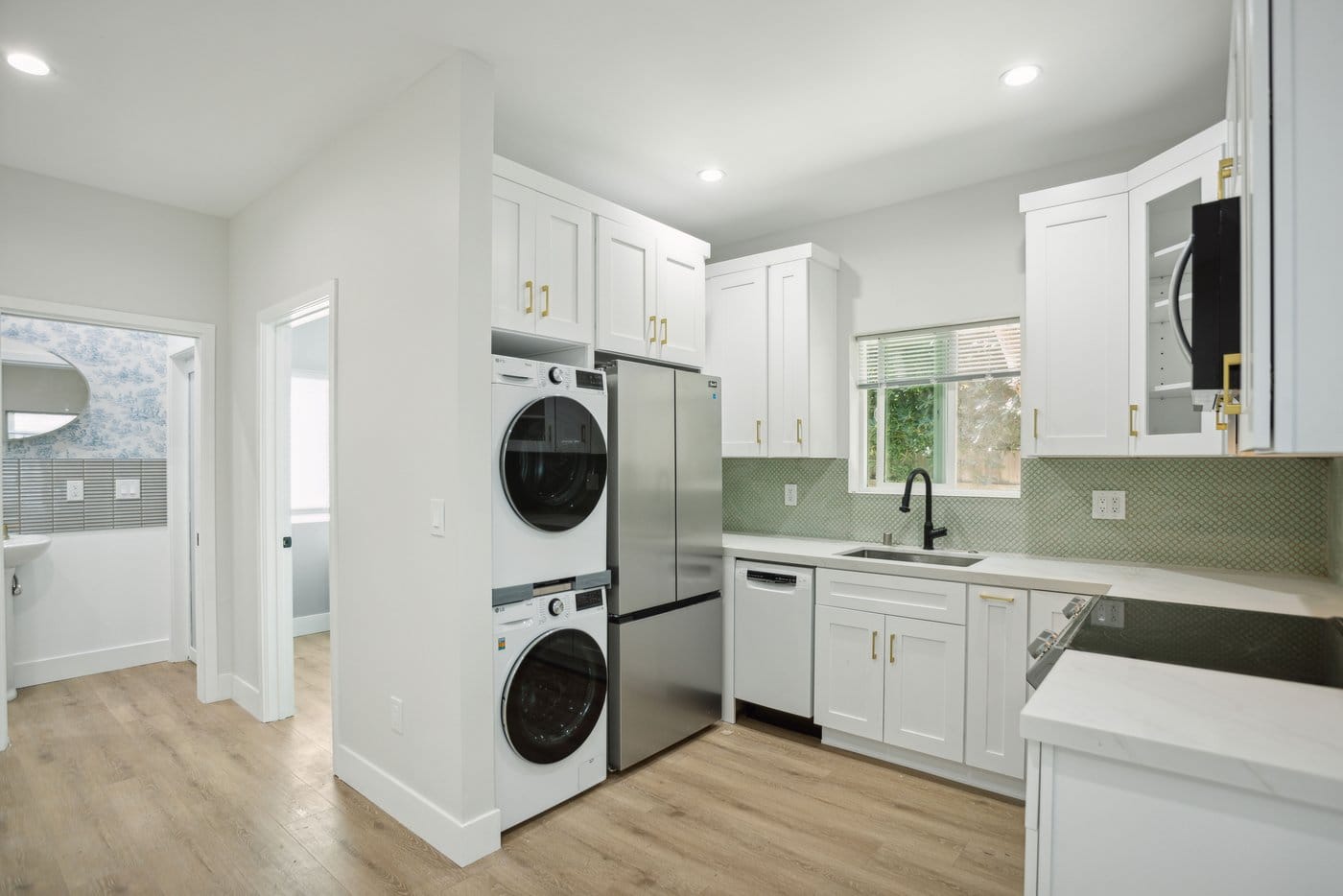 White shaker kitchen with stainless appliances and a green tiled backsplash, seen from the living area
