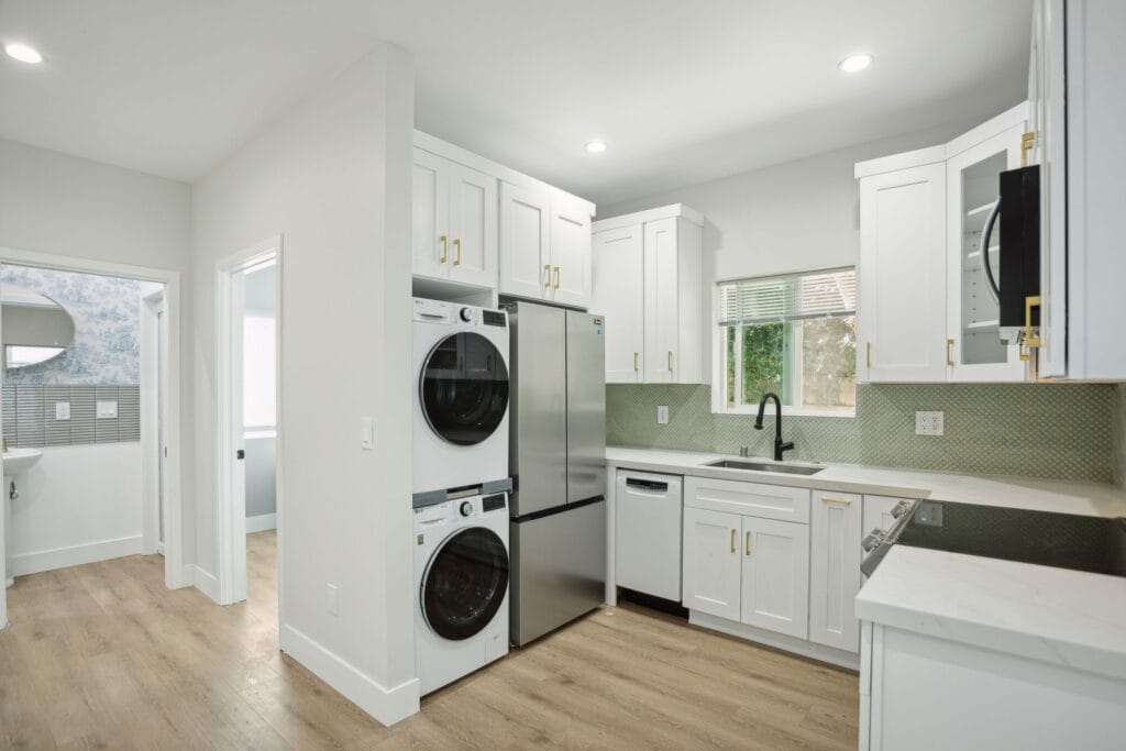 The same kitchen from the living side, refrigerator and laundry stack together, a bathroom doorway beyond