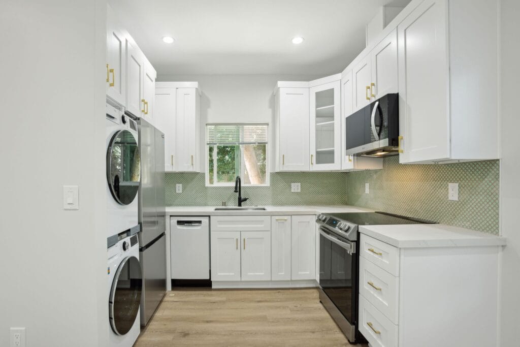 Compact white shaker kitchen with a stacked washer and dryer built into the run, and a pale green glass splashback