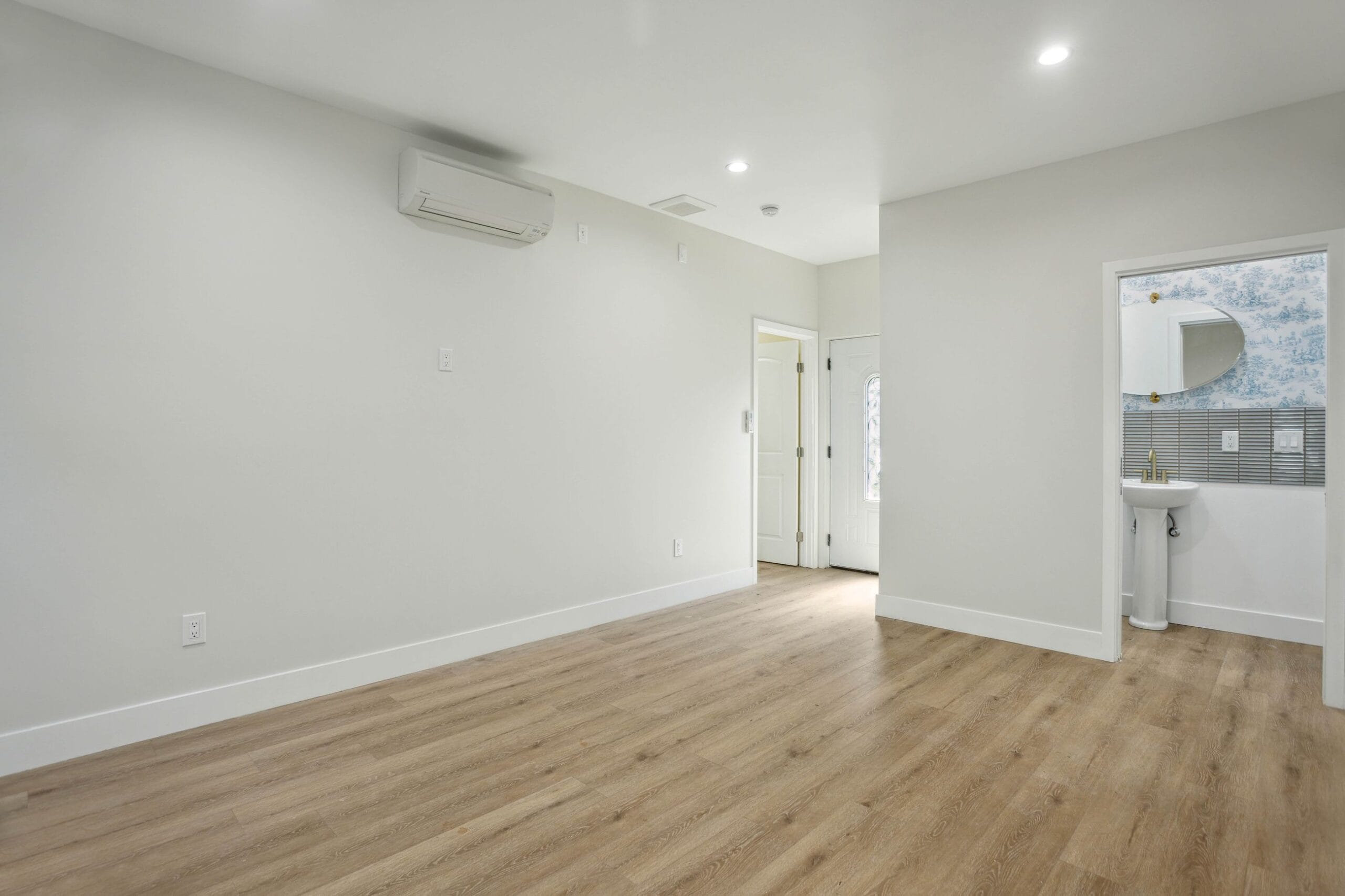 Living area with a wall-mounted mini-split head, recessed lighting and a doorway through to the bathroom