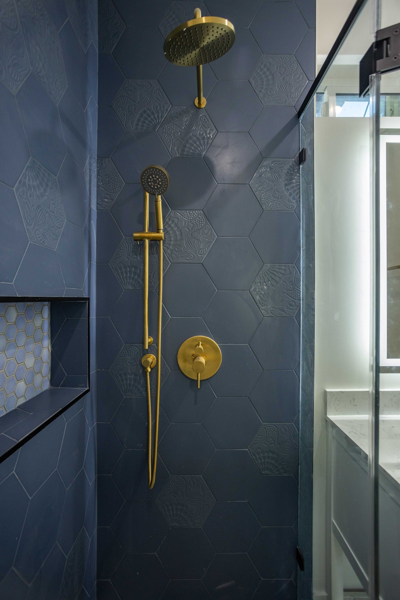 Brass shower riser, rain head and handheld against navy hexagonal wall tile