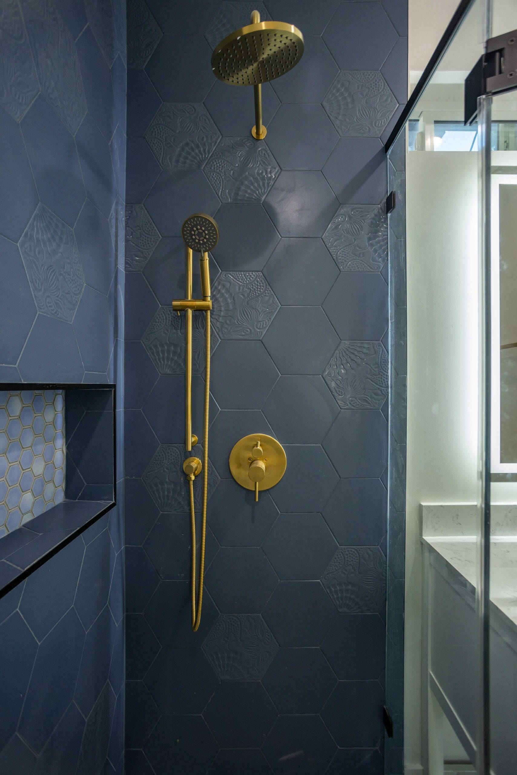 Brass shower riser, rain head and handheld against navy hexagonal wall tile