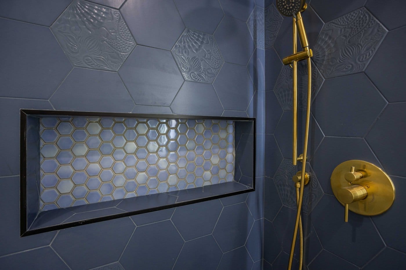 Mosaic-lined recessed niche and brass fittings set into a navy hexagonal tiled shower wall