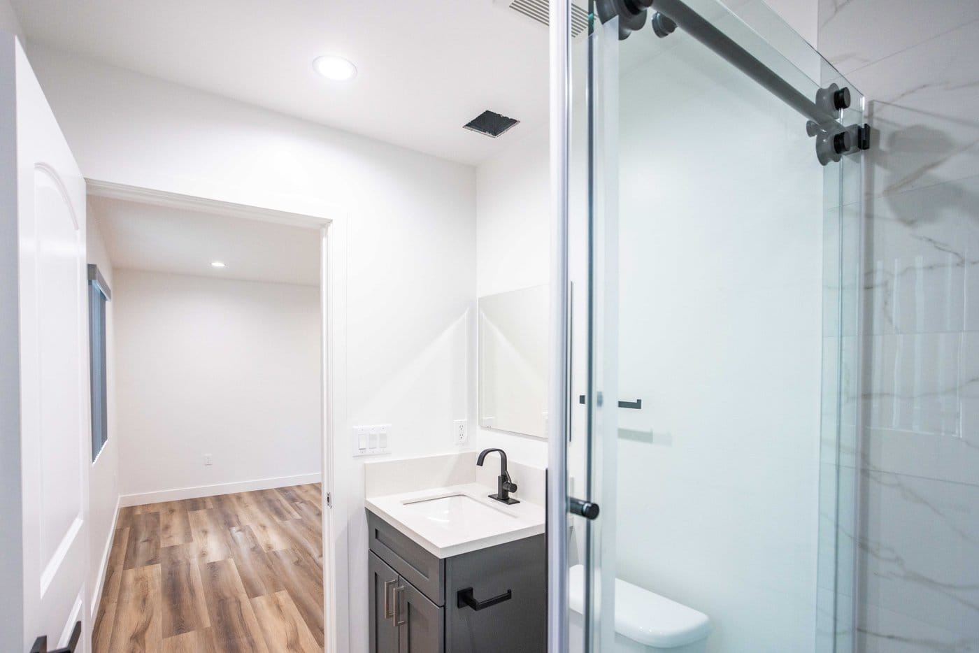 Converted garage bathroom looking out past the vanity and glass shower to the adjoining room