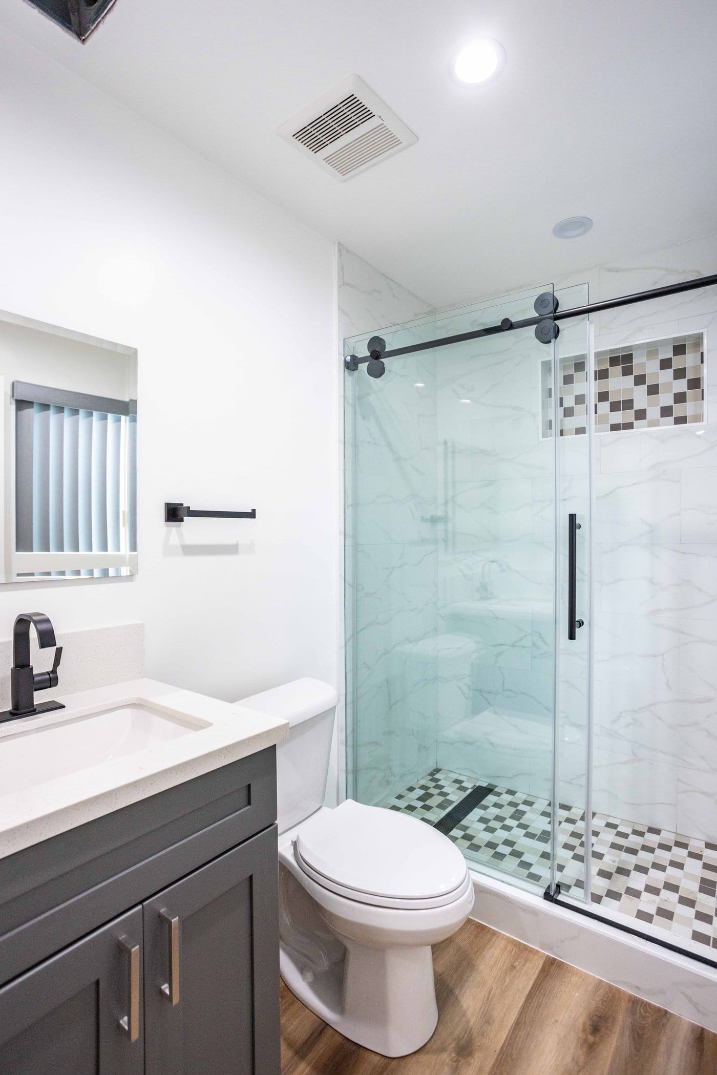 Bathroom with a dark shaker vanity and white stone top, black tapware, a sliding glass shower door on a black track and marble-effect porcelain wall tile