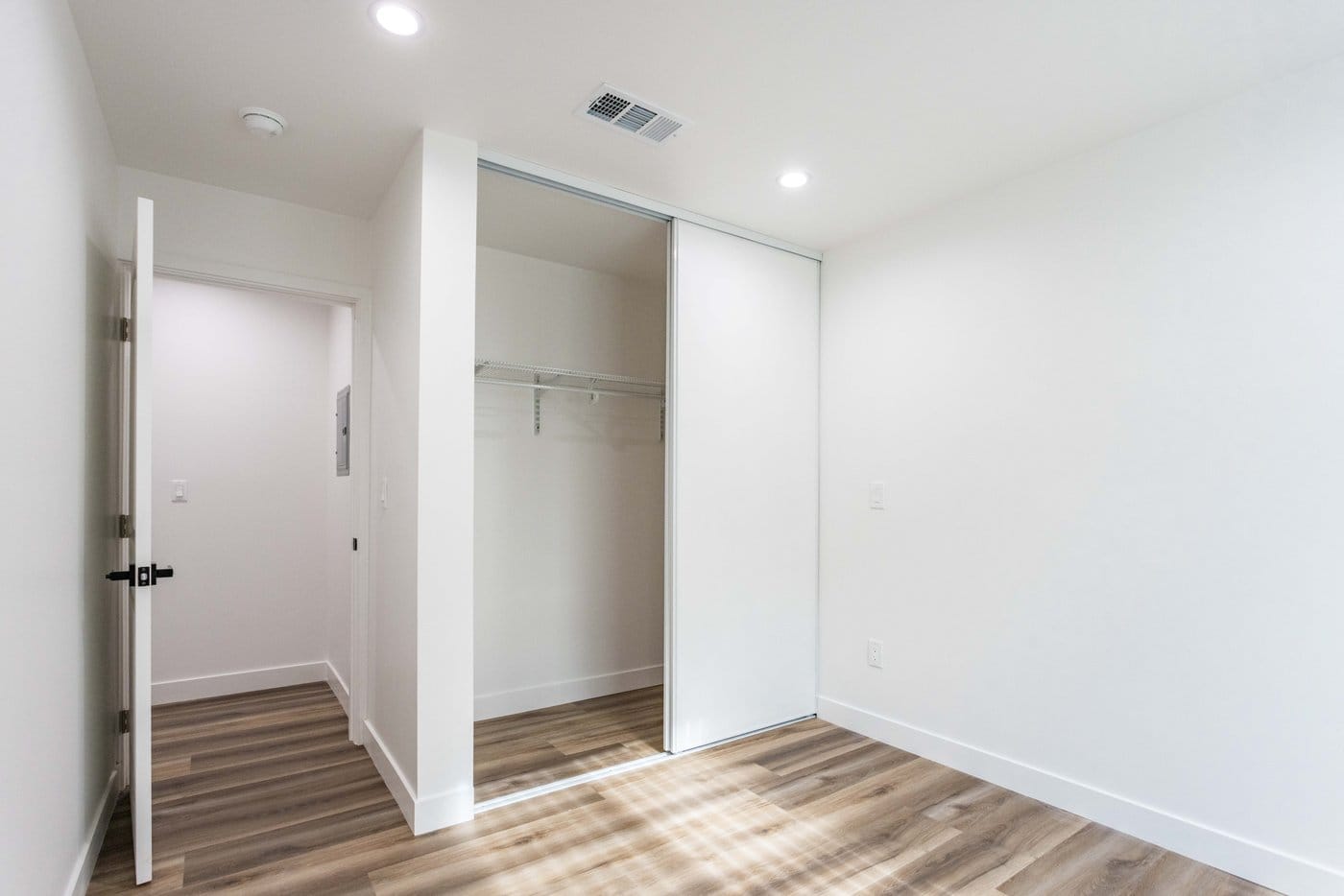 Mirrored sliding closet doors standing open to a hanging rail, beside a doorway and wood-look plank flooring