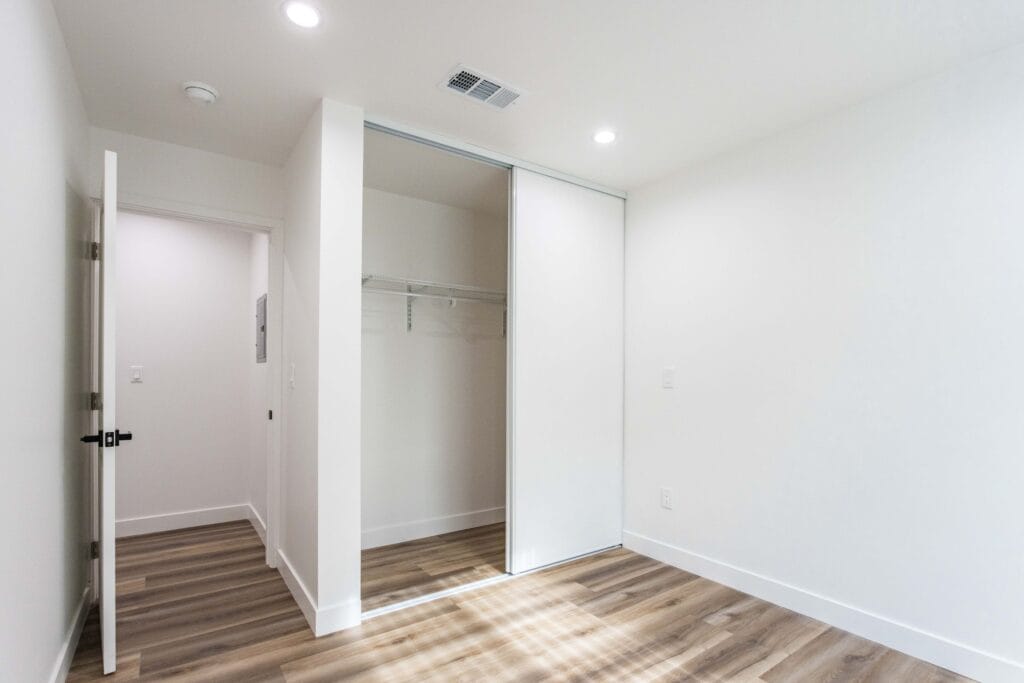 Mirrored sliding closet doors standing open to a hanging rail, beside a doorway and wood-look plank flooring