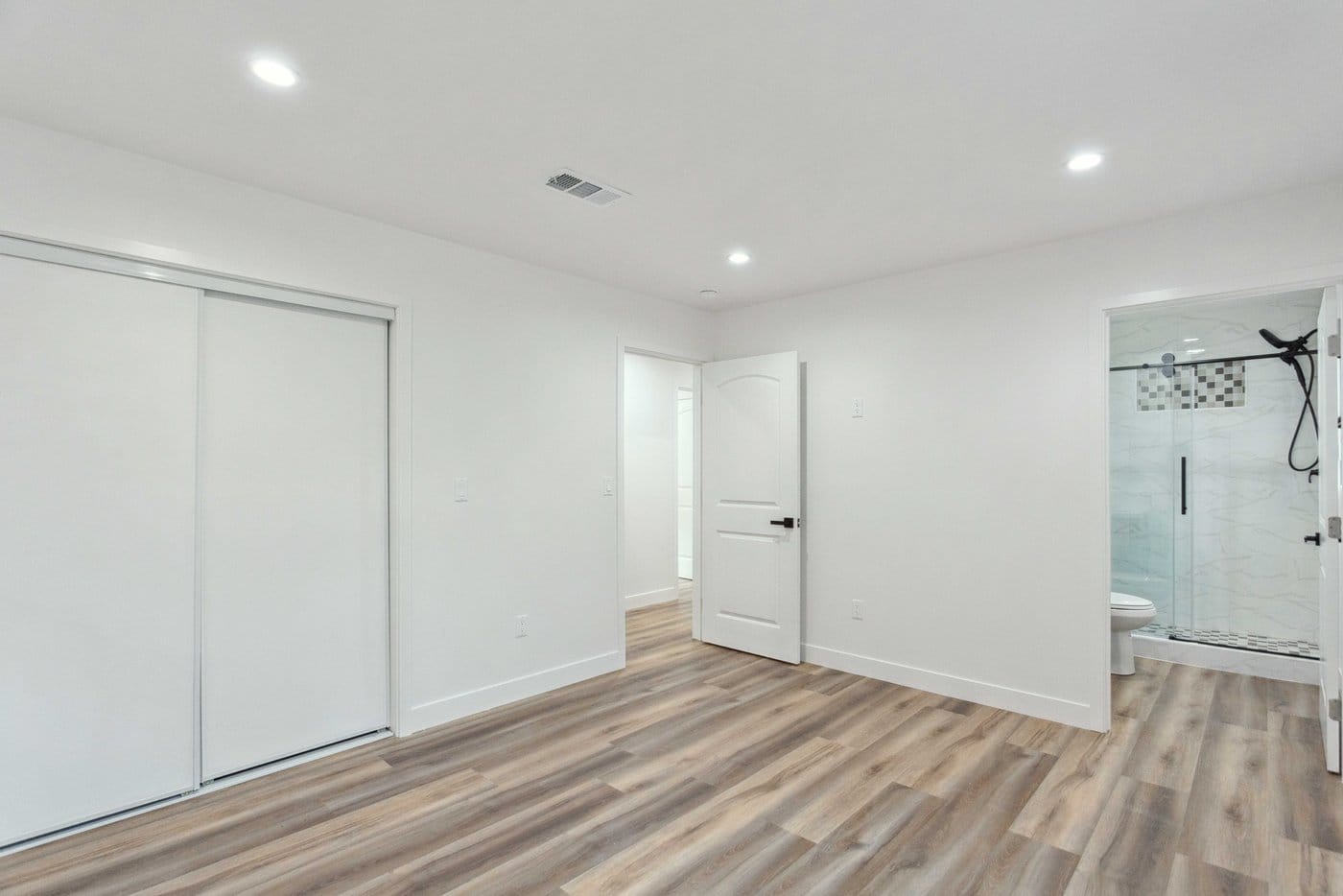Finished interior of a converted garage with mirrored sliding closet doors, wood-look plank flooring and an open doorway through to the bathroom