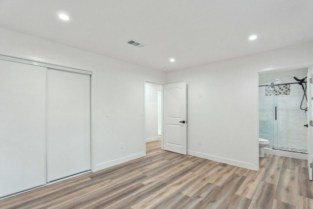 Finished interior of a converted garage with mirrored sliding closet doors, wood-look plank flooring and an open doorway through to the bathroom