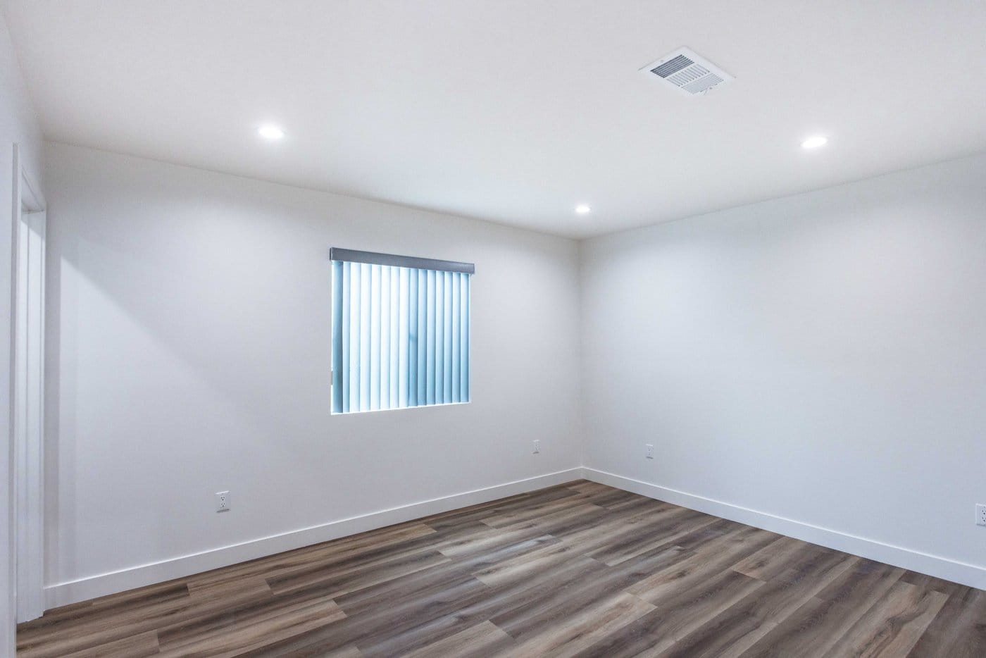 Empty finished room with a white-framed window, vertical blinds, recessed lighting and wood-look plank flooring