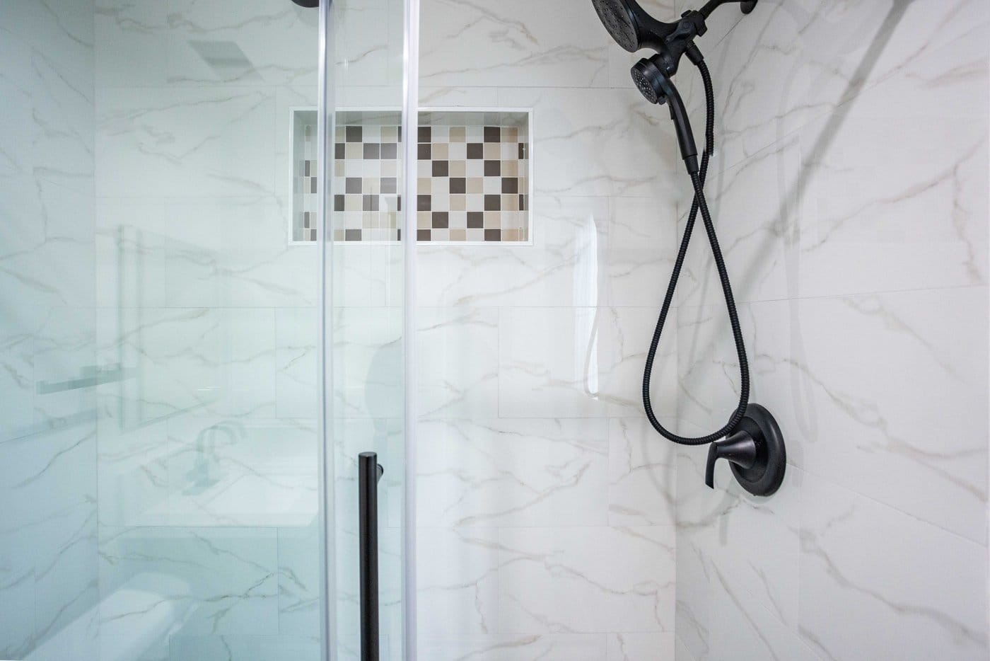 Shower detail with marble-effect porcelain walls, a recessed mosaic-lined niche and matte black rain head, handheld and valve