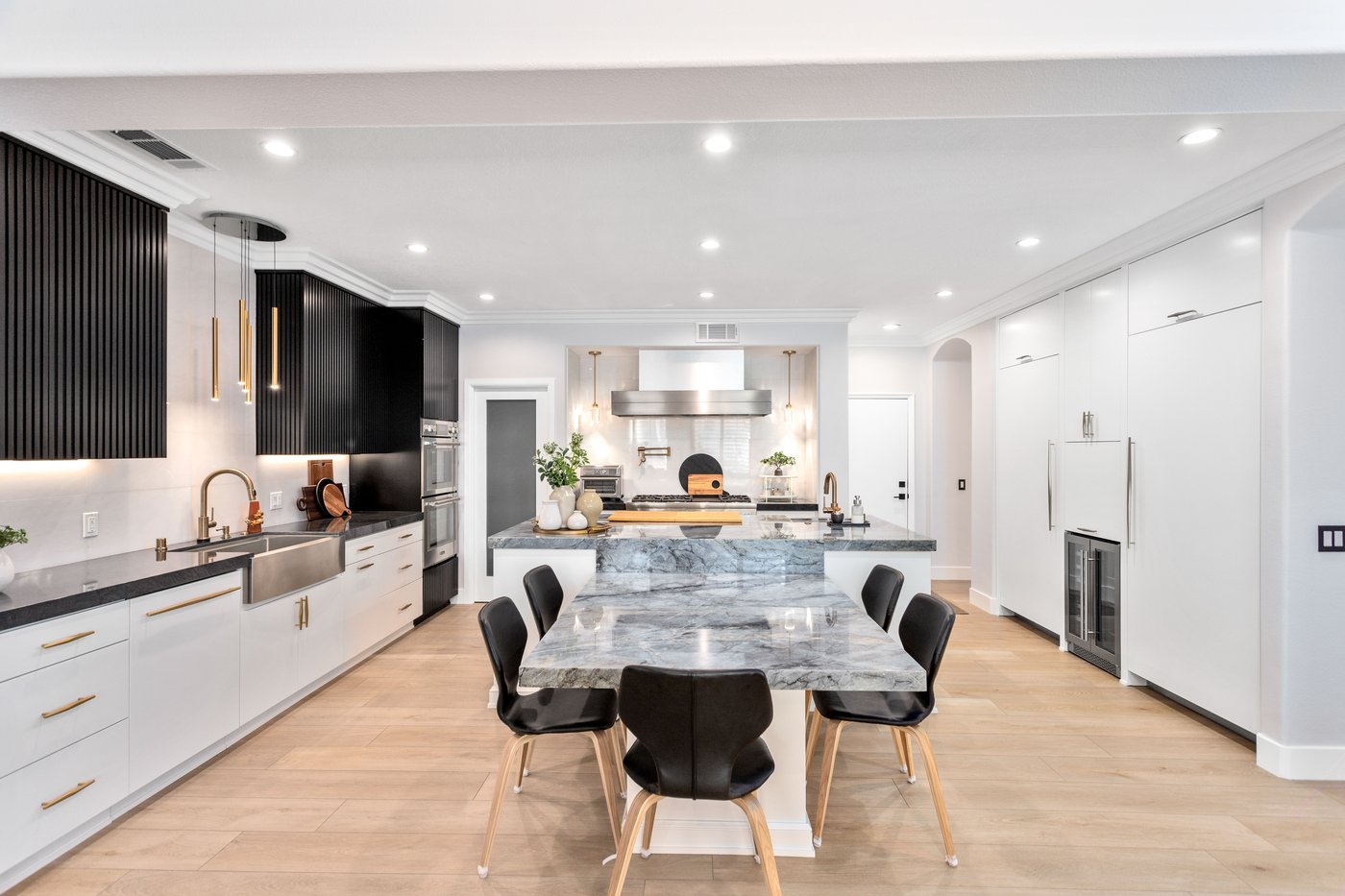 Kitchen with white cabinetry, dark upper units and a marble island seen across the dining table