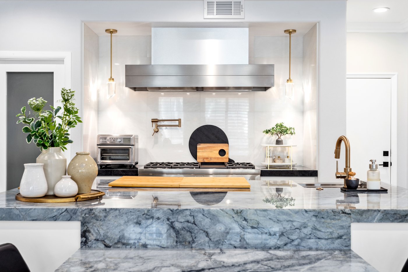 Cooking wall with a stainless range, wall-mounted hood and marble splashback between tall cabinetry