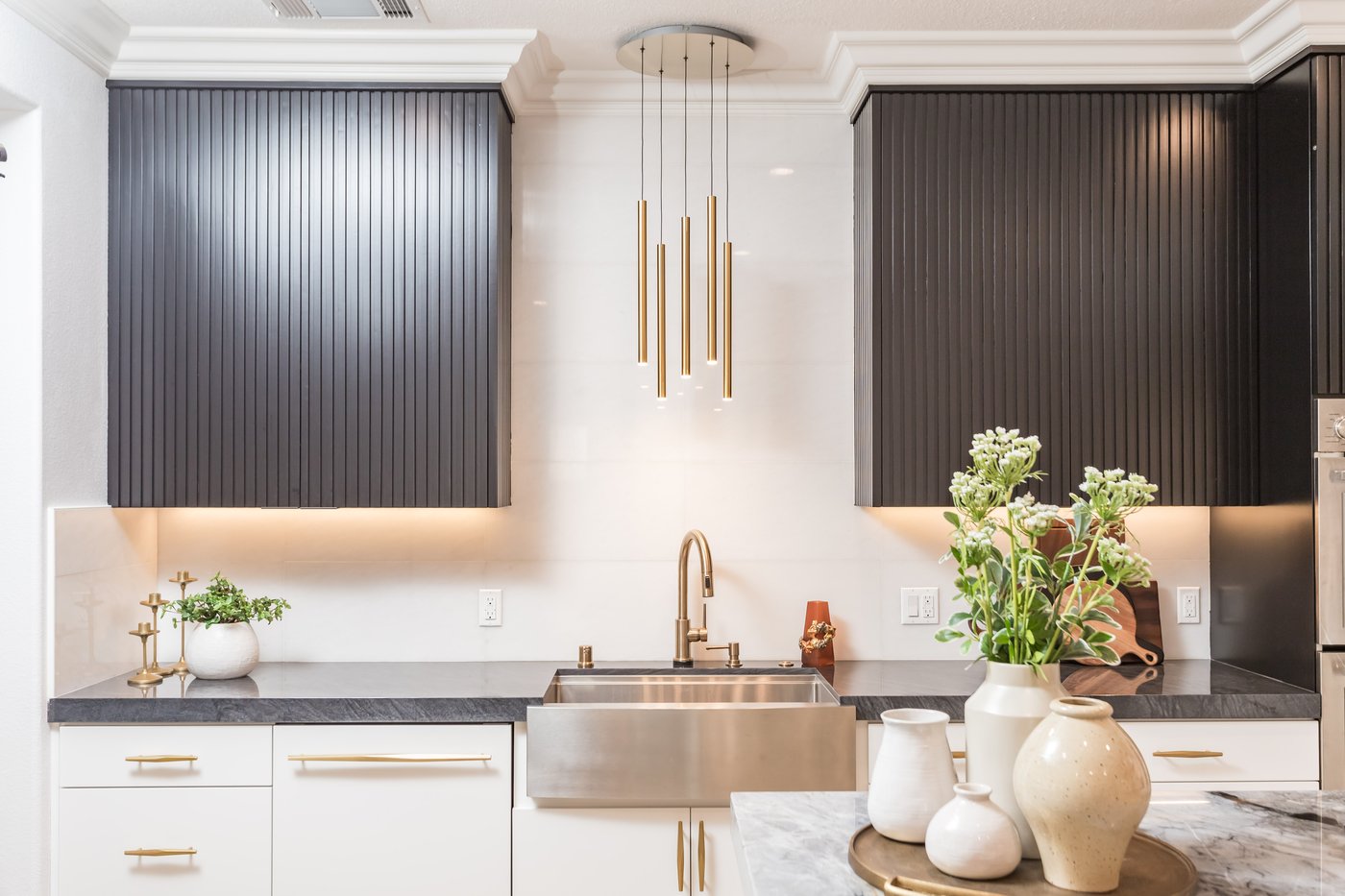 Farmhouse sink under pendant lighting against a fluted dark cabinetry backdrop