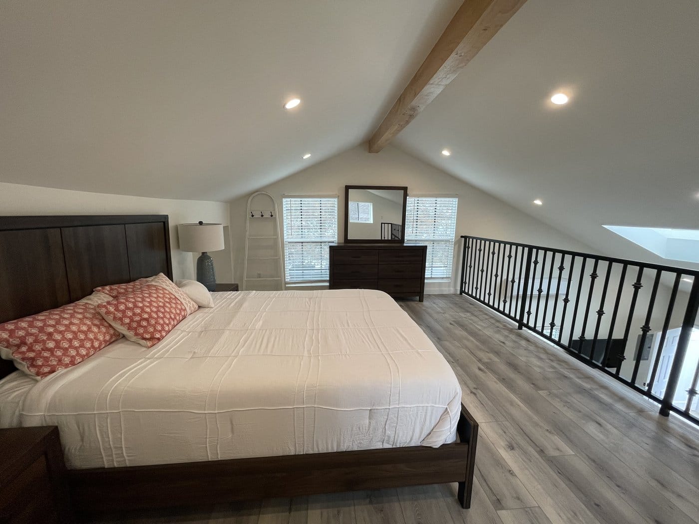 ADU loft bedroom under a vaulted ceiling with an exposed timber beam, open to the railing above the living area