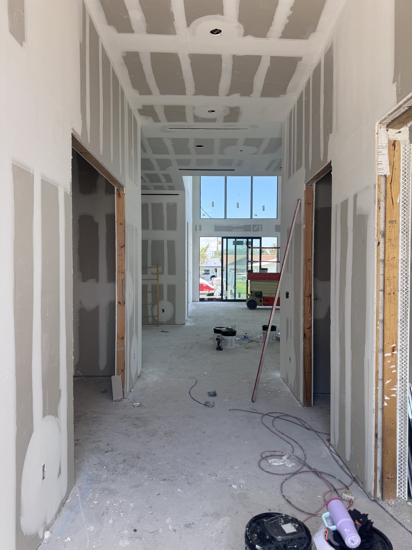 Interior corridor at drywall stage with taped joints, unfinished floor and daylight from the far opening