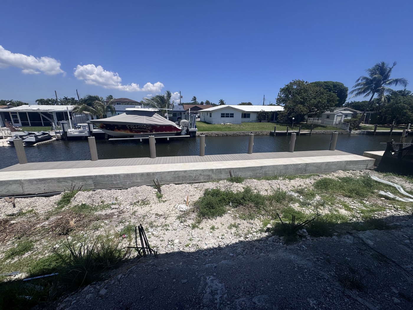 Cleared and filled waterfront building lot with a concrete seawall along the canal and neighbouring houses beyond