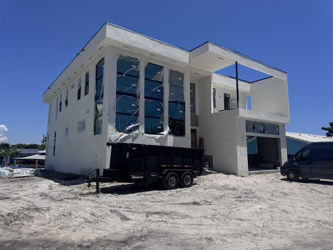 Completed structural shell of a two-storey waterfront house with glazing installed, on a prepared and levelled lot