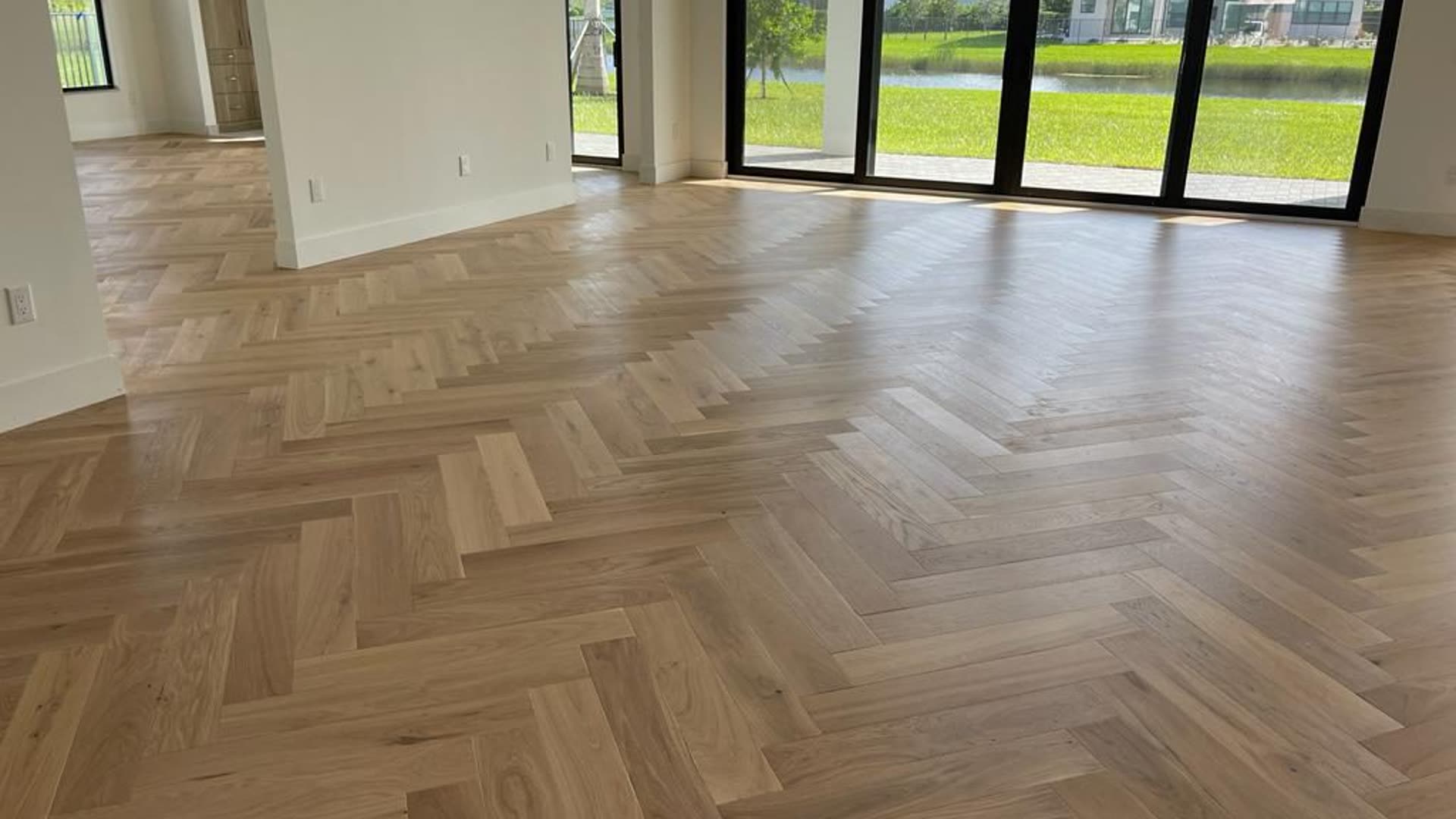 Pale oak herringbone floor running the length of a great room with a full-height black-framed glazed wall