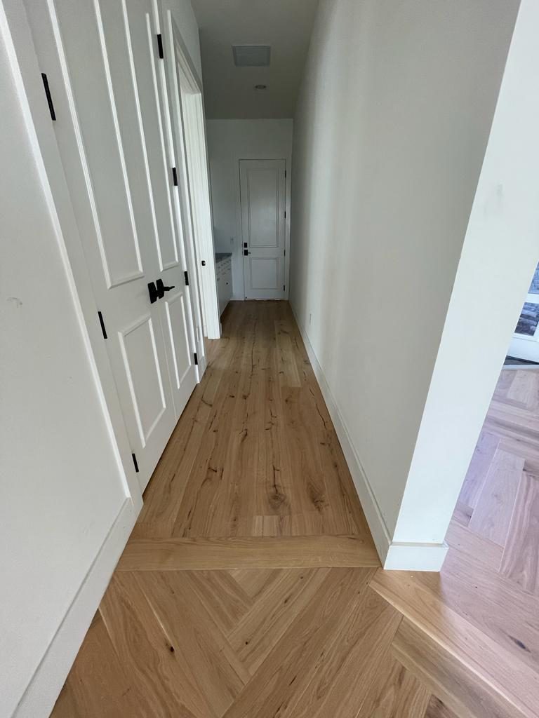 Herringbone floor running down a hallway and meeting a straight-laid border at the threshold