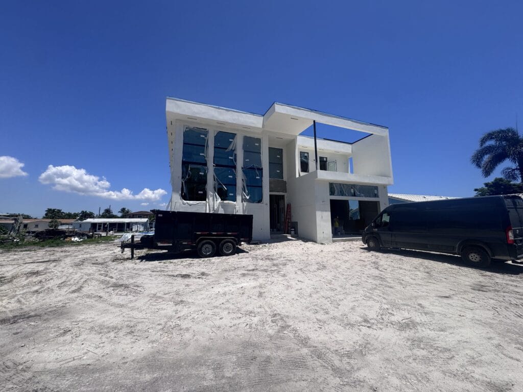 A rough-graded waterfront lot with a two-storey house set back from the canal, built by Elbaz Construction in South Florida