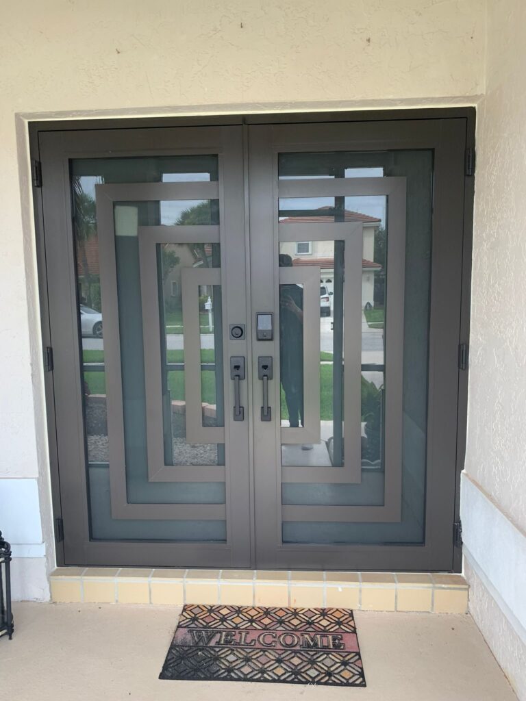 Grey double entry door with obscured glazed panels and a matching frame, set into a rendered wall under a covered entry