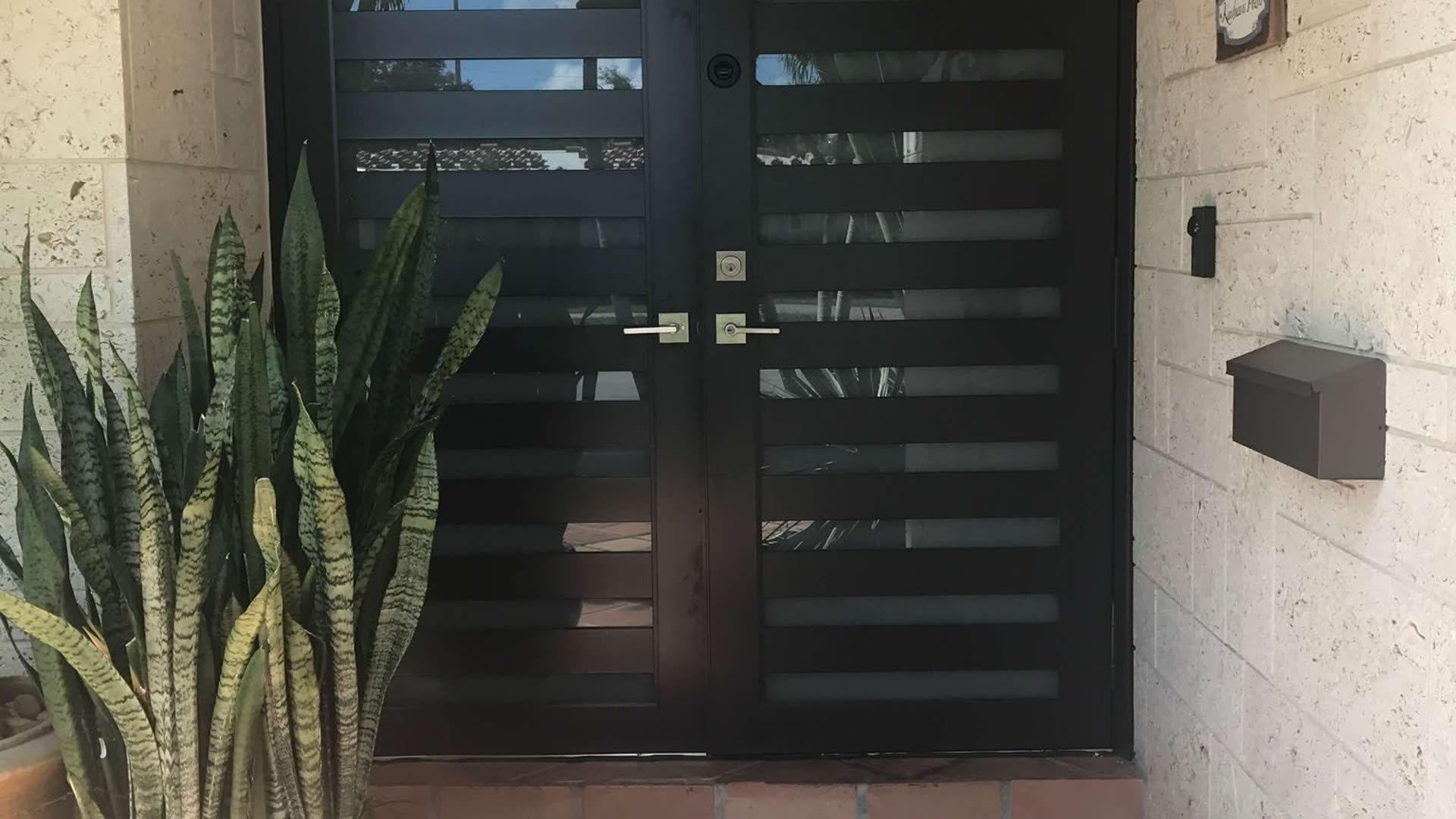Grey double entry door with obscured glazed panels and a matching frame, set into a rendered wall under a covered entry