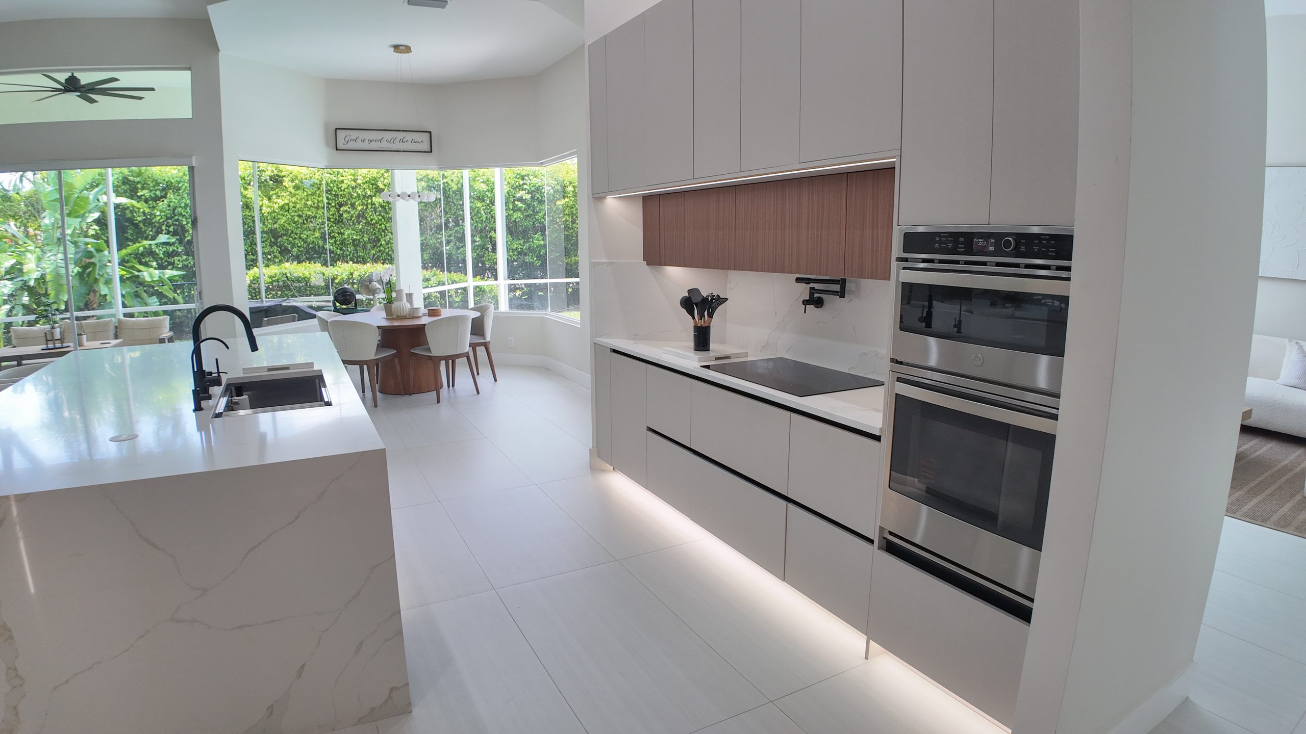 The cooking wall: induction hob, twin ovens and lit shadow-gap under the timber cabinets