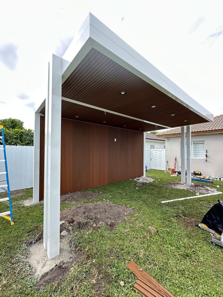 Covered outdoor structure part-built on open ground, showing the frame, the timber soffit lining and the ground still to be surfaced