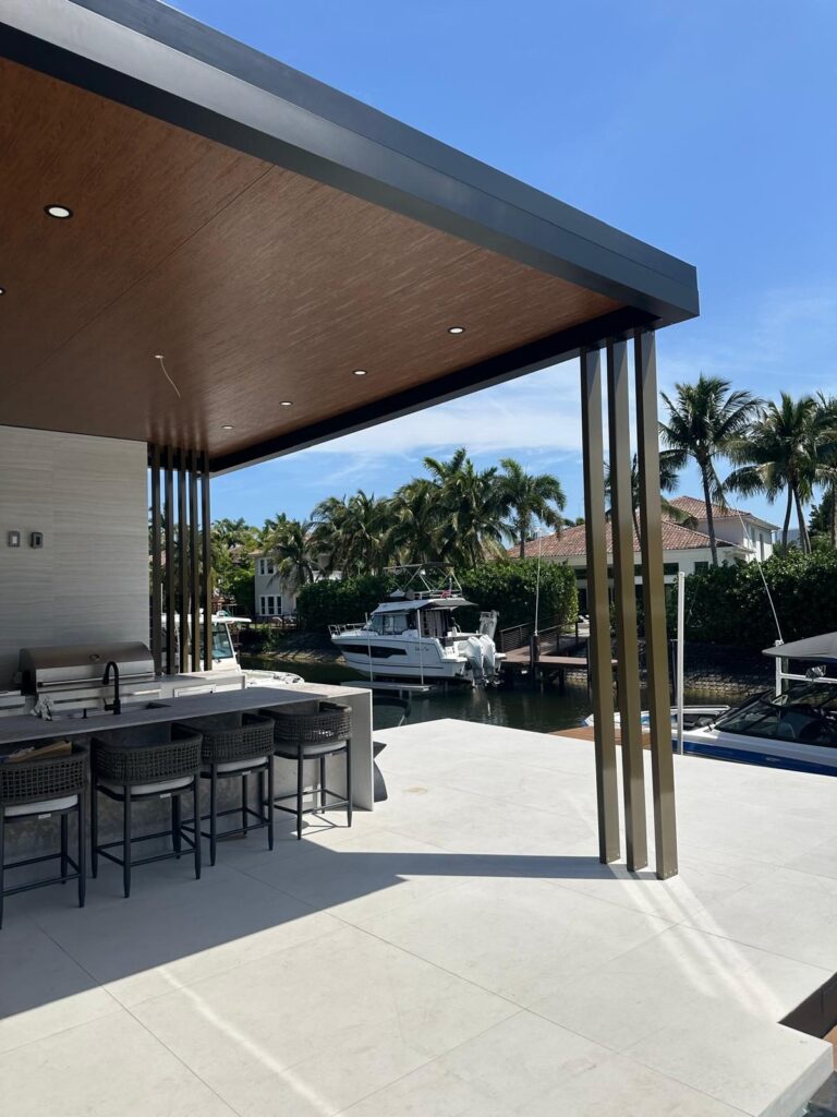 Outdoor kitchen counter and bar stools under a deep covered roof, with boats moored beyond