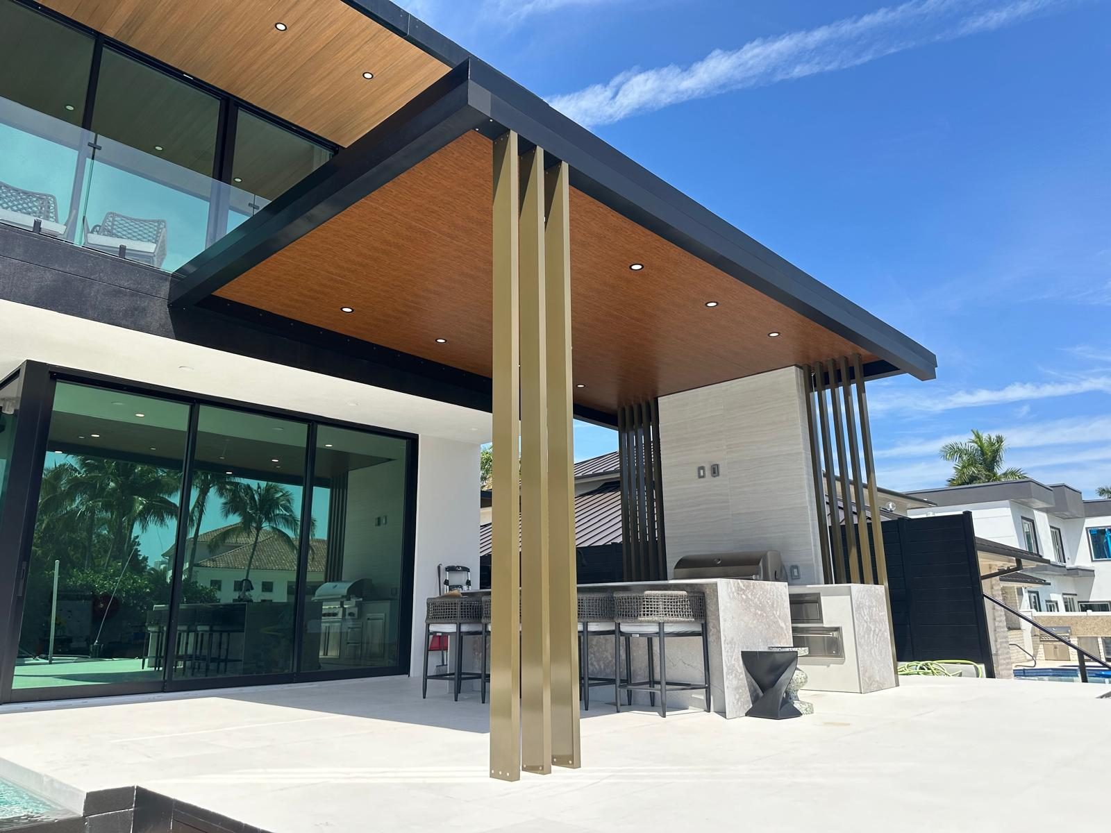 Outdoor kitchen with bar seating beneath a cantilevered covered structure attached to the rear of a house