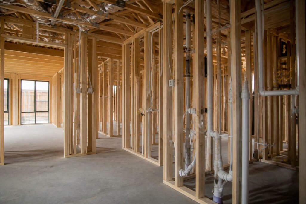 Illustration of a residential interior at rough-in stage with framing, wiring, pipework and ducting exposed before boarding