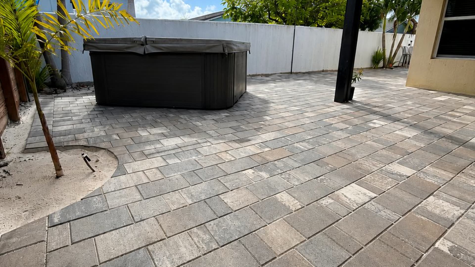 Large-format paver terrace laid around a sunken spa beneath a thatched shade structure, with a rendered boundary wall behind