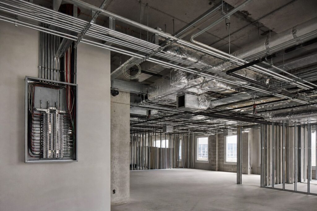 Illustration of commercial services rough-in: conduit, cable tray, ductwork and a distribution board exposed before the ceiling is closed