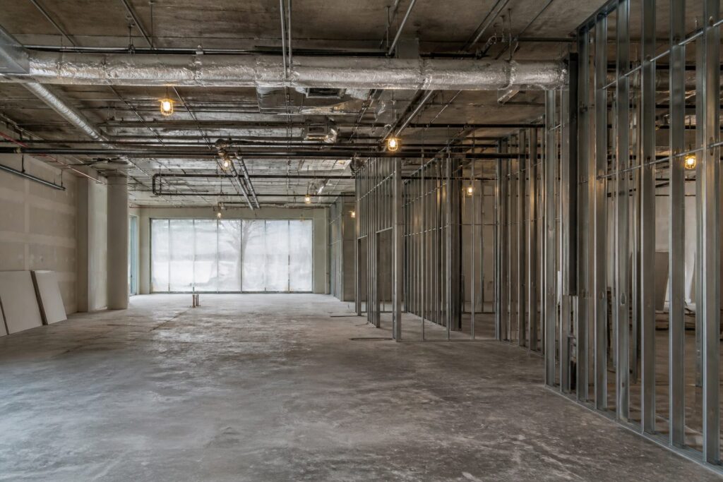 Illustration of an empty retail unit at shell stage: bare floor, exposed structure and services overhead, new stud partitions part-built
