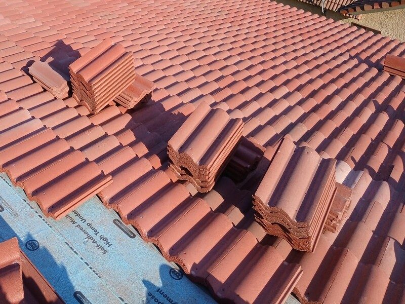 Barrel tile courses being laid over underlayment with further tile stacked on the roof ready to run
