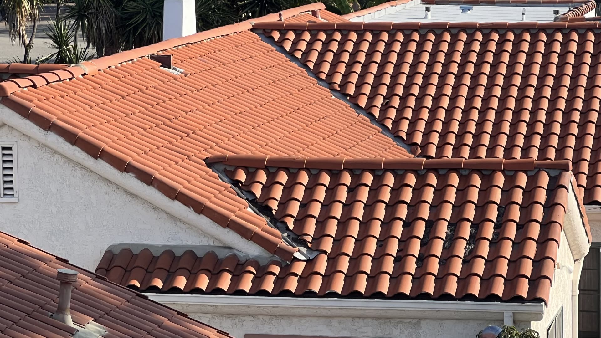 Completed terracotta S-tile roof over white stucco walls, showing hip and ridge lines across several roof planes