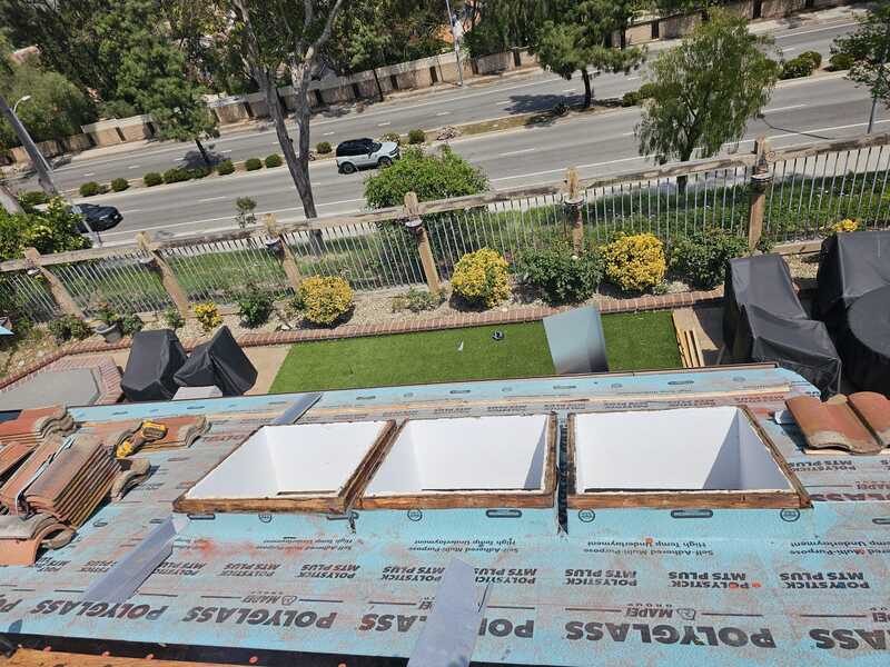 Wide view of a roof dried in with self-adhered underlayment, three skylight curbs formed, and tile stock staged along the edge