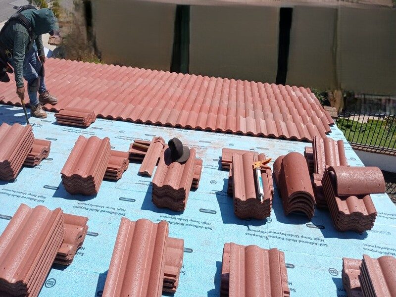 Barrel tile stacked across an underlaid roof deck and the first courses being set from the eave upward