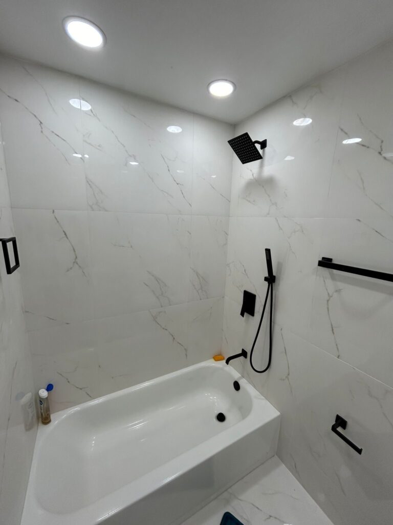 Bath with a shower over it, tiled in marble-look porcelain with matt black fixtures — the arrangement most conversions start from