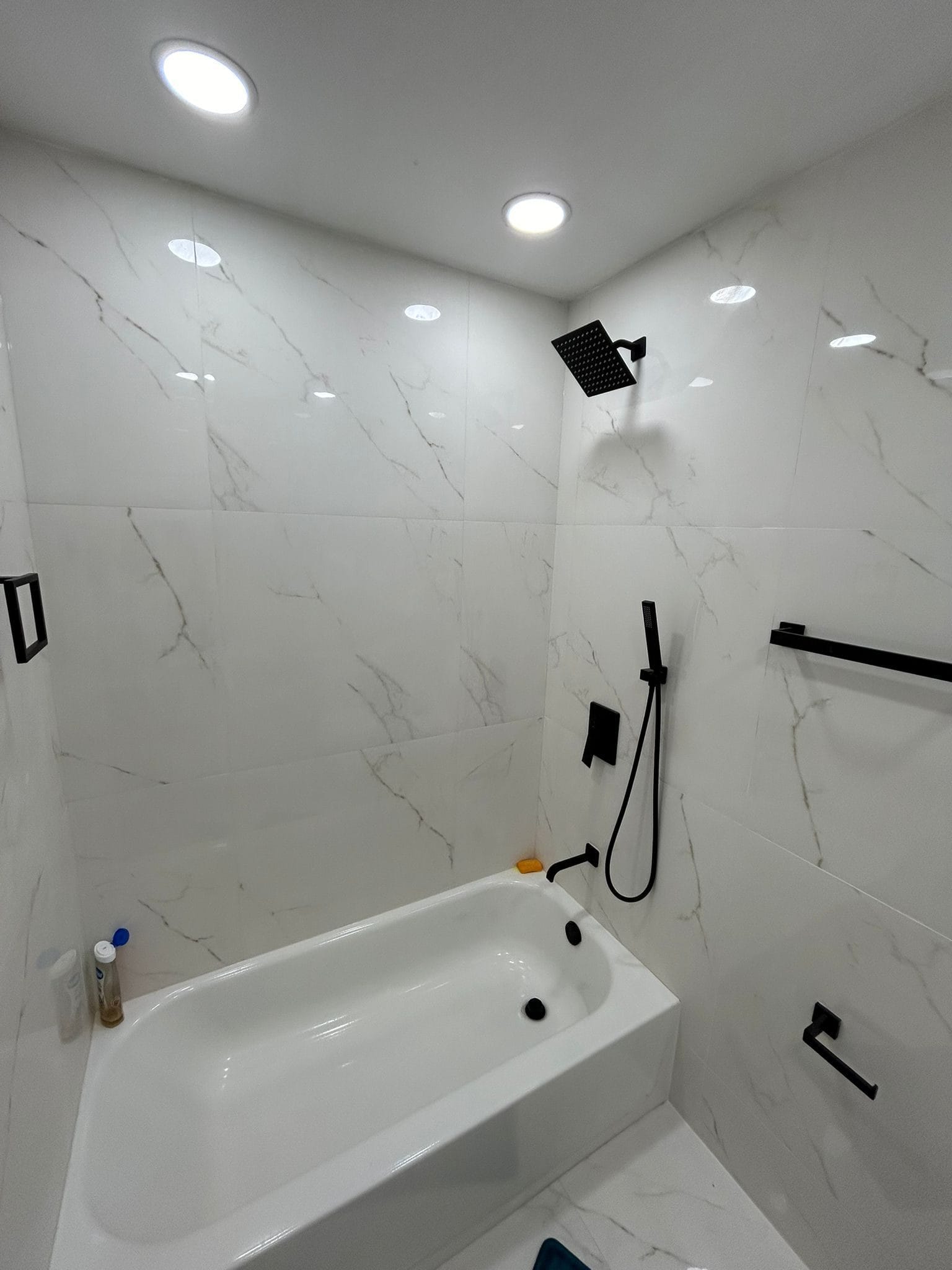 The original bathroom before conversion: a bath and shower combination against marble-look tile