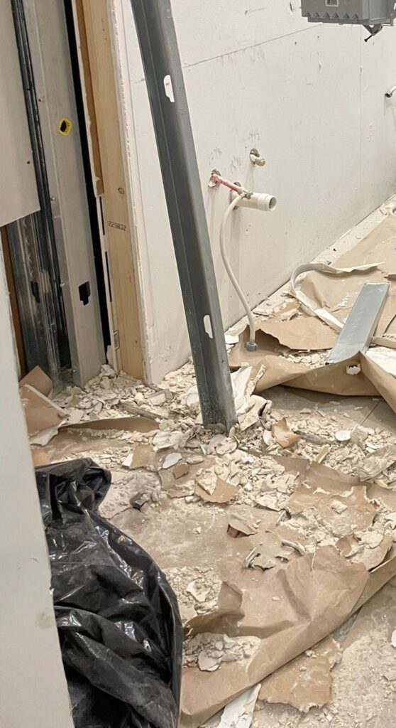 Bathroom stripped back during demolition, with the wall board removed, supply pipework exposed and debris still on the floor